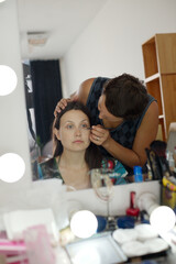 Caucasian young adult woman sitting at makeup station receiving eye makeup from Caucasian young...
