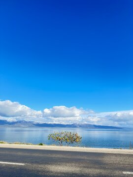 Calm waters mirror the snow-dusted mountains and drifting clouds beneath a brilliant blue sky, capturing the peaceful harmony of nature where earth, water, and sky unite in quiet perfection.