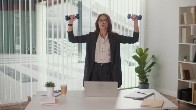 Office Ergonomics and Employee Wellbeing. Office Manager Performs Shoulder and Upper Spine Exercise with Dumbbells at Desk to Improve Posture, Prevent Pain, Support Productivity and Corporate Wellness