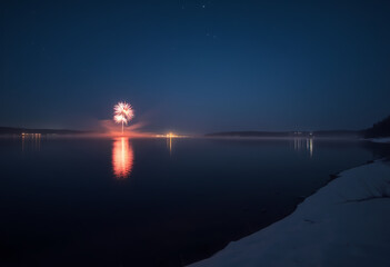 Nighttime fireworks display over water with snowy shoreline