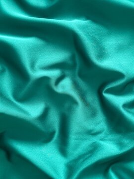Smooth emerald green satin fabric with elegant folds and soft reflections, creating a luxurious and silky texture that shines beautifully under light, perfect for fashion, design, or interior inspirat