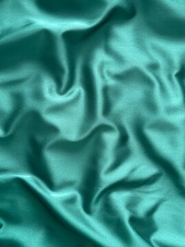 Smooth emerald green satin fabric with elegant folds and soft reflections, creating a luxurious and silky texture that shines beautifully under light, perfect for fashion, design, or interior inspirat