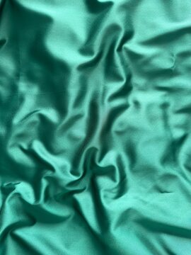 Smooth emerald green satin fabric with elegant folds and soft reflections, creating a luxurious and silky texture that shines beautifully under light, perfect for fashion, design, or interior inspirat