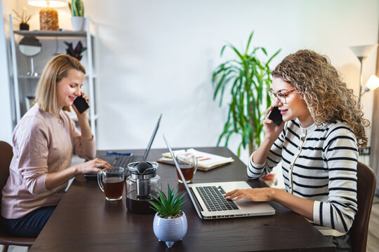 Two businesswoman working at a desk on laptop and talking on a phone call