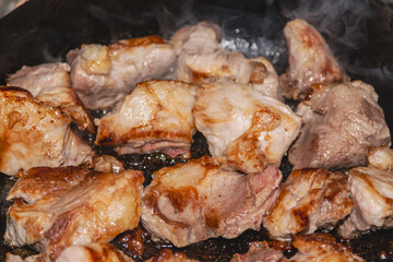 Pieces of frying meat in a pan with light smoke rising from cooking, close-up. Fried meat in a pan
