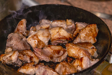 Pieces of various frying meat in a pan on a kitchen stove, close-up.