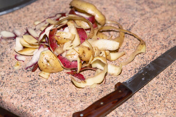 Potato peels gathered in a pile on a kitchen table next to a kitchen knife, close-up. Peeling and preparing potatoes