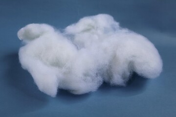 Soft white Dacron fibers displayed on a smooth blue background, highlighting their fluffy and...