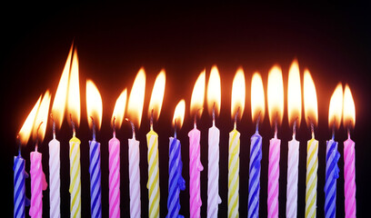 Different birthday cake candles burning on black background