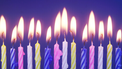 Close up of many colourful birthday cake candles burning on blue background