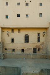 Plain textured wall in Fes, Morocco, featuring several small window openings scattered irregularly. Ideal architectural background showcasing Moroccan simplicity and traditional earthen tones.