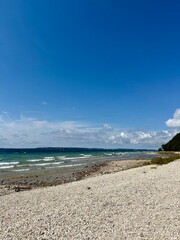 Rocky shoreline with gentle waves and turquoise water along Mackinac Island, Michigan, under a bright blue summer sky.