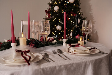 A festive holiday table setting with lit candles, wine glasses, and a Christmas tree in the background