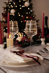 A festive holiday table setting with lit candles, wine glasses, and a Christmas tree in the background