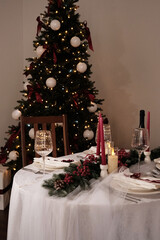 A festive holiday table setting with lit candles, wine glasses, and a Christmas tree in the background