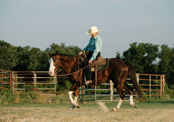 Cowgirl western lifestyle with woman riding horse outside in Texas field.