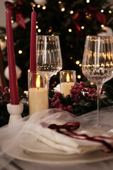 A festive holiday table setting with lit candles, wine glasses, and a Christmas tree in the background
