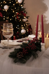 A festive holiday table setting with lit candles, wine glasses, and a Christmas tree in the background