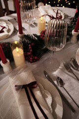 A festive holiday table setting with lit candles, wine glasses, and a Christmas tree in the background
