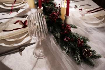 A festive holiday table setting with lit candles, wine glasses, and a Christmas tree in the background