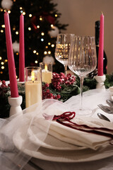 A festive holiday table setting with lit candles, wine glasses, and a Christmas tree in the background