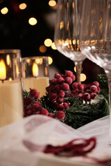 A festive holiday table setting with lit candles, wine glasses, and a Christmas tree in the background