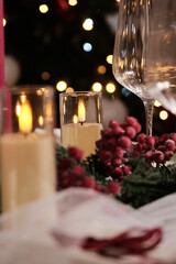 A festive holiday table setting with lit candles, wine glasses, and a Christmas tree in the background