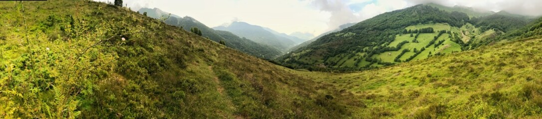 Fototapeta premium Expansive panorama of lush green valley surrounded by mountainous landscapes