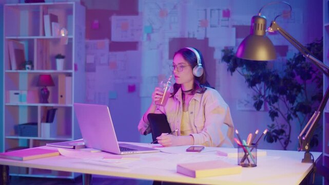 Mindful Creativity, Emotional Focus, Gen Z Style. Woman in Headphones Sketches in Neon Room at Night While Listening Music. Personal Moment of Inspiration, Calm, and Expressive Flow