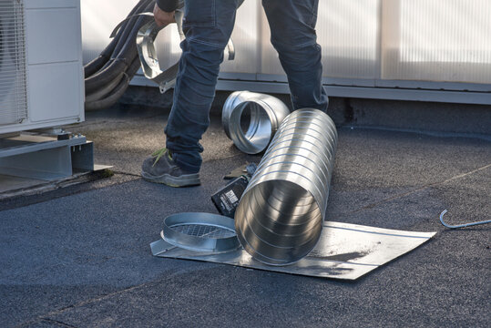 Technician working on an industrial rooftop installing galvanized ventilation ducts. HVAC system installation, air extraction, and industrial maintenance concept.