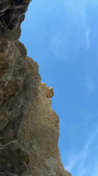 Dramatic rock formations under blue sky, camera pans upward revealing heights
