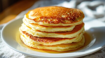 A tall stack of fluffy pancakes sits on a white plate glistening with syrup ready to be enjoyed.