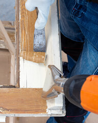 Carpenter using heat gun and wood scraper removes paint from old wooden window. Construction industry, carpentry. Restoration. 