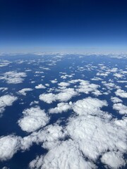 High-altitude aerial cloudscape with endless white cumulus clouds floating over the deep blue ocean and a crisp horizon line under a clear sky, perfect for travel, freedom, and atmospheric concepts.