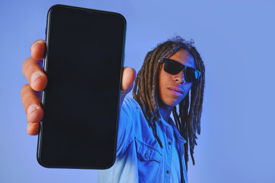Young man wearing dreadlocks and sunglasses holding up a smartphone with an empty screen