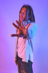 Young man with dreadlocks expressing a stopping gesture with his open palm on a gradient background