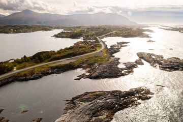 Atlantic ocean road reveals narrow track winding across rocky islands creating dramatic connection across sea. Norwegian landscape under overcast sky