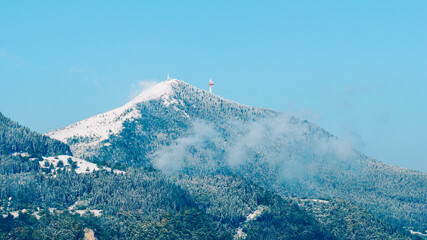 Snowy mountain peak with communication tower under clear blue sky, bright winter day with sunlight and scattered clouds