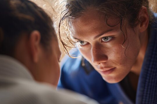 Close-up of focused female jiu-jitsu athletes in gis locked in intense grappling, sweat and determination captured during training