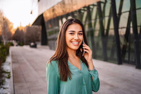 Young businesswoman smiling while using smartphone in front of modern office building - Powered by Adobe