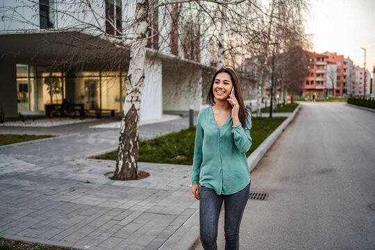 Young woman walking down the street while talking on smartphone