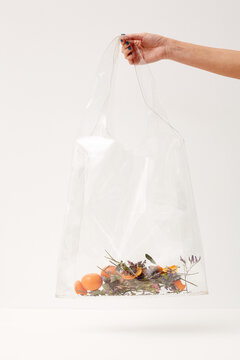 Hand of unrecognizable woman holding transparent plastic bag with herbs, tangerine skin and tangerines in it