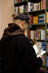 Stylish young man in cap browsing book in bookstore.