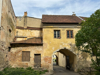 Vilnius, Lithuania, September 4, 2025, A cobbled courtyard through a crumbling archway in a weathered yellow building with a tiled roof, showing exposed brick and peeling plaster.