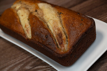 Sliced banana bread rests on a white plate, showing its rich brown color and golden crust. The sweet aroma fills the air, inviting everyone to enjoy this delicious treat.