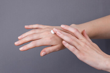 Woman applying moisturizing cream on hands, Close-up of female hands applying white moisturizing cream on skin, showing skincare, hydration, softness, and personal care routine.