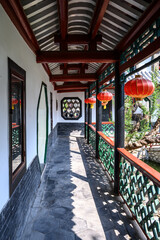 A corridor in a traditional Chinese courtyard with red lanterns hanging outdoors.