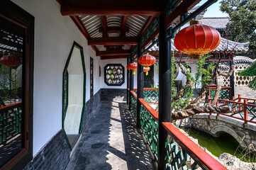 A corridor in a traditional Chinese courtyard with red lanterns hanging outdoors.