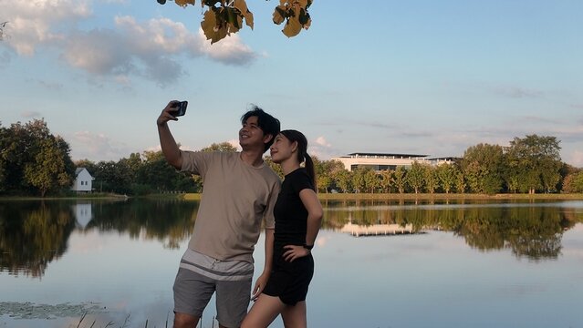 A man and woman are taking a selfie in front of a lake