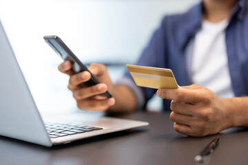 A close-up photo of the hands of a young man in an office, sitting in front of a laptop, holding a credit card and a phone